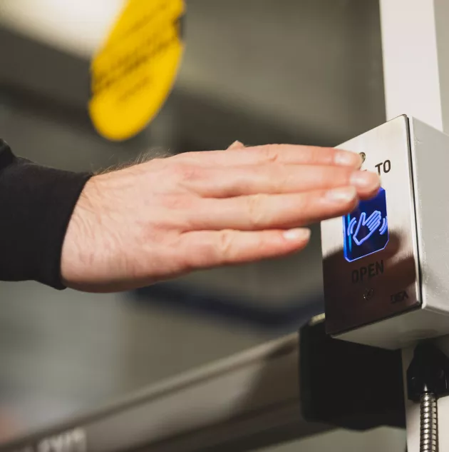 A person waving near a button to open an accessible door.