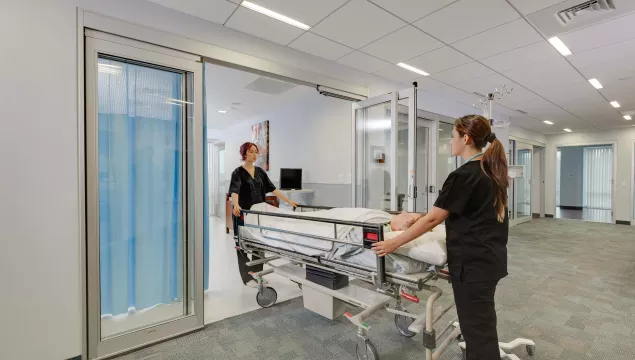 A hospital bed wheeled out of a set of doors.